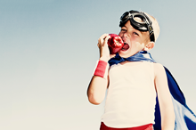 boy eating an apple with a cape on