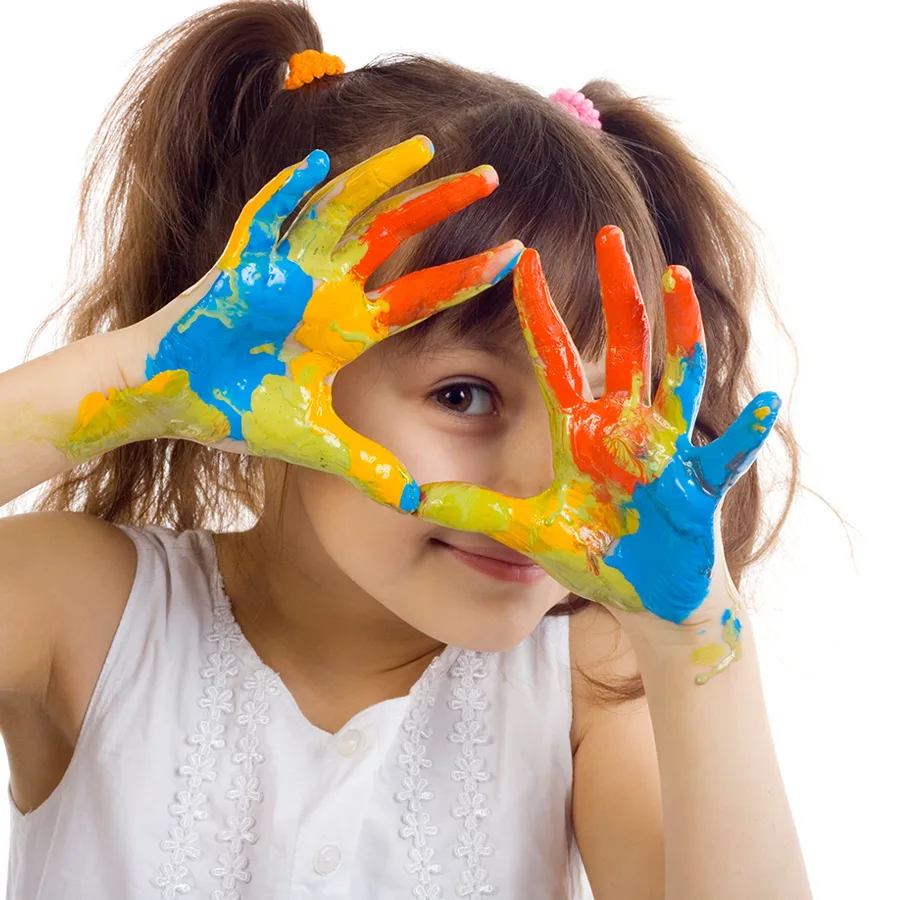 A young girl in pigtails holding up hands messy with fingerpaint