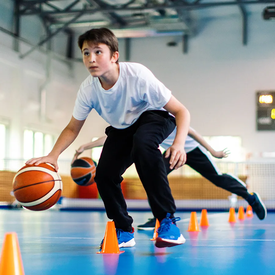 A teenage boy dribbles a basketball between cones