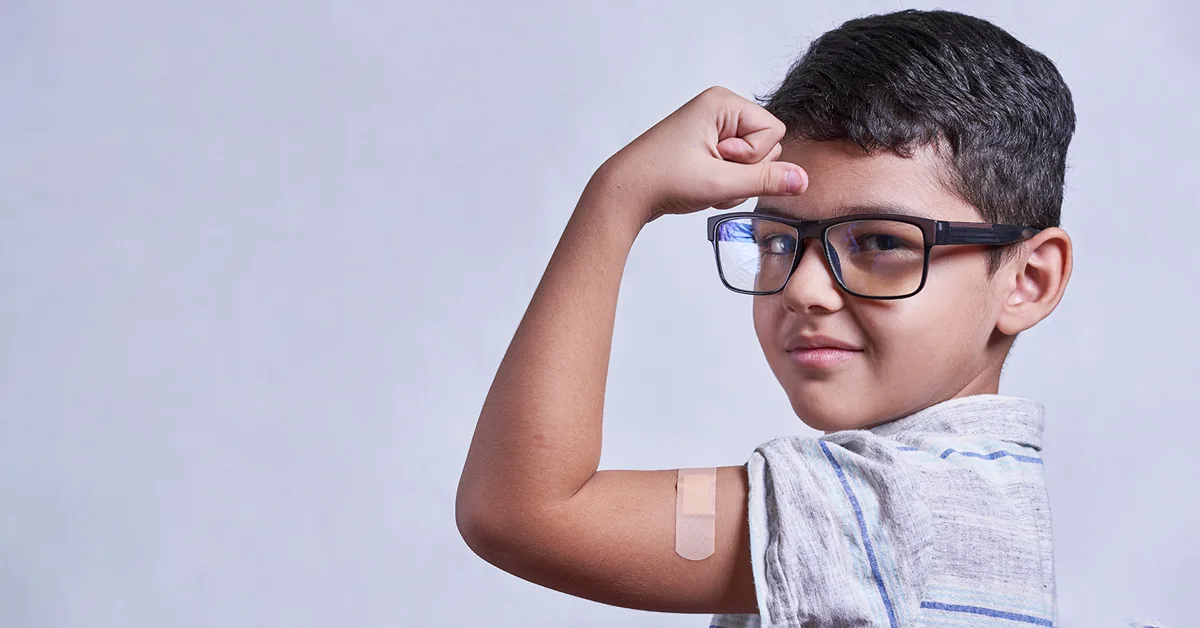 A young boy in classes flexing his bicep featuring a band aid