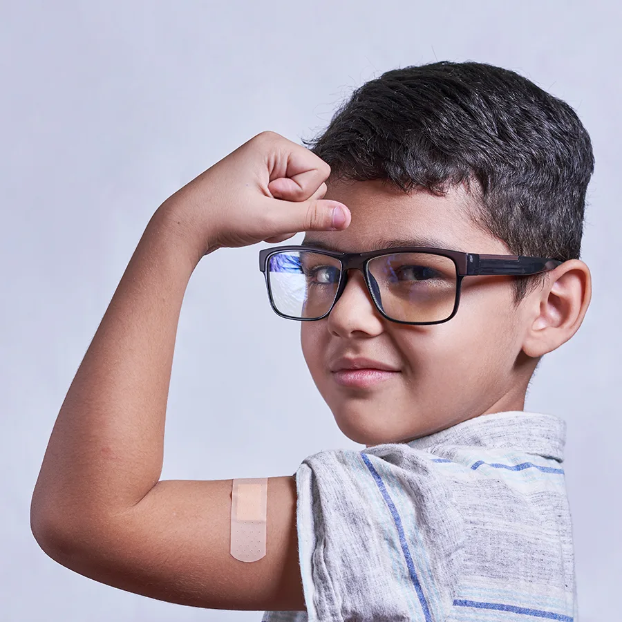 A young boy in classes flexing his bicep featuring a band aid