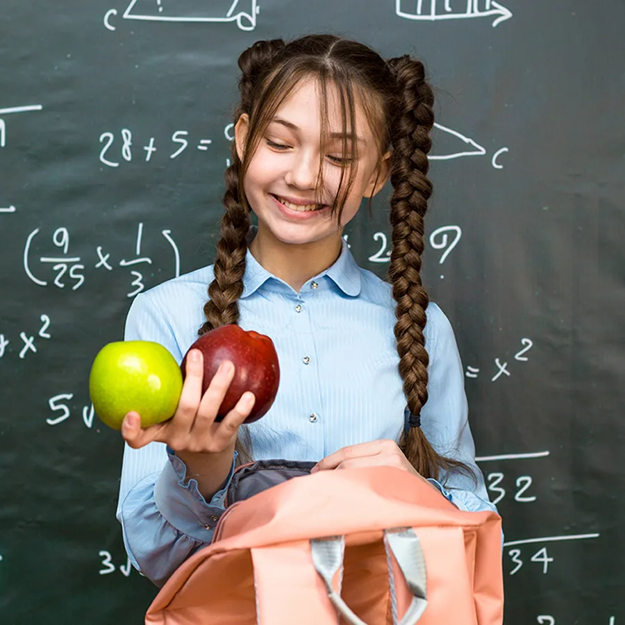 A teenage girl in braids smiles at the fruit she is holding