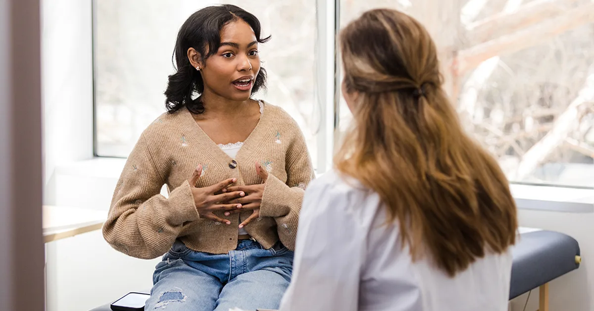 A teenage girl in a sweater talks to a medical professional