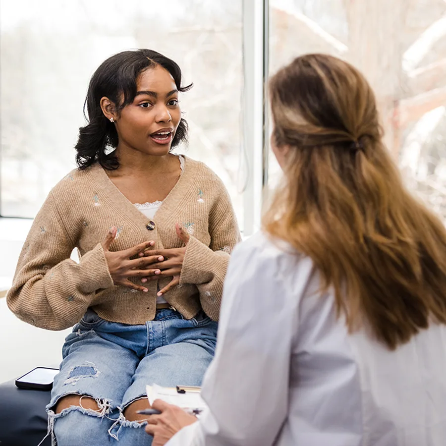 A teenage girl in a sweater talks to a medical professional